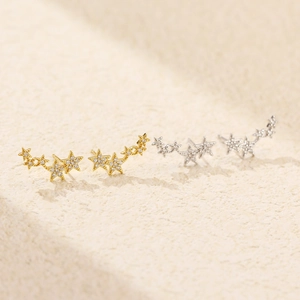 Macro shot of silver and gold star earrings with pavé crystals on beige background