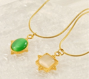 Détail du collier à chaîne serpent dorée avec pendentifs en pierre œil de chat vert et blanc