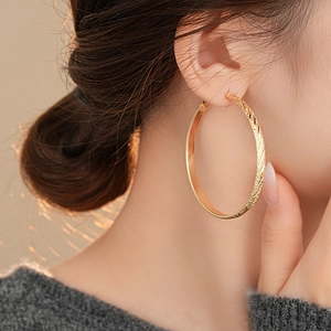 Makroaufnahme großer goldener Creolen mit eleganter Twill-Gravur für Frauen
