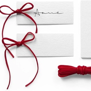 Detail von eleganten roten Samtbändern, als Schleifen an weiße Geschenkanhänger gebunden