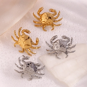Macro detail of crab shaped earrings in gold and silver plating on white textured background
