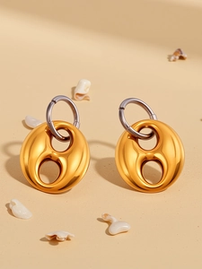 Macro detail of gold and silver two-tone earrings on sand with white seashell accents