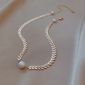 Elegant gold leaf chain necklace with a single large pearl pendant on beige silk