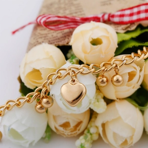 Macro shot of polished gold heart charm and small beads on stainless steel bracelet