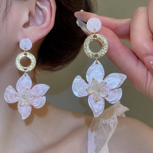 Nahaufnahme von rosa Harzblumen-Ohrringen mit goldenen Hammerschlag-Ringen am Model