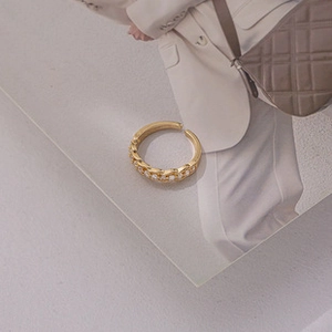Close-up of golden chain-link ring with zircon inlay on a mirrored surface