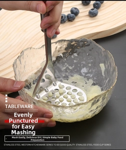Manual stainless steel potato masher with round holes pressing food in a glass bowl