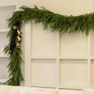 Norfolk pine garland with gold bells and dark ribbon hung on a white door frame
