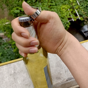 Action shot of a stainless steel ring bottle opener opening a beer bottle cap on a thumb