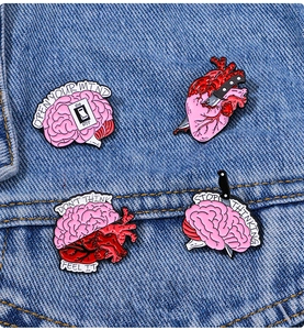Detail of four creative anatomical heart and brain enamel pins on denim fabric