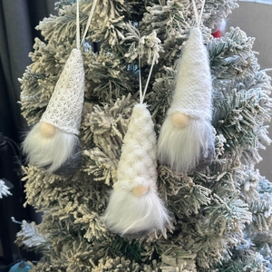 Three Christmas gnome hanging ornaments with white and gray knits on a snowy tree
