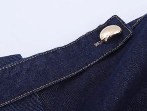 Nahaufnahme von dunkelblauem Denim-Stoff mit einem goldenen Knopf in Schotenform