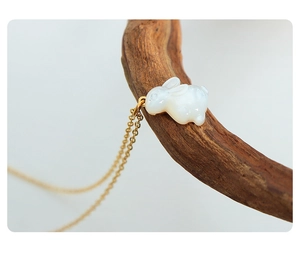 Gros plan d'un pendentif lapin blanc sur une chaîne dorée posé sur une branche en bois