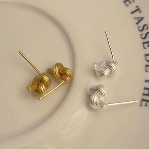 Detailed view of silver and gold knot stud earrings on a cream ceramic tray