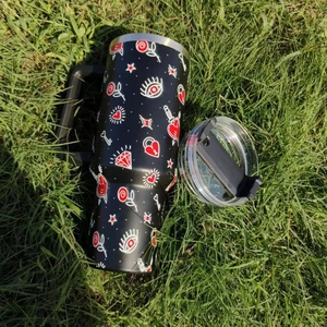 Outdoor top view of a 40oz black tumbler with tattoo patterns on green grass