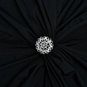 Détail d'une broche fleurie argentée avec strass brillants sur tissu plissé noir