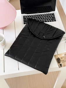 Nahaufnahme der schwarzen gesteppten Laptoptasche auf Schreibtisch mit modernem Zubehör