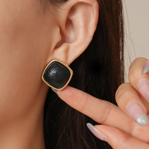 Macro view of geometric leather earrings with gold metal frame on model's ear
