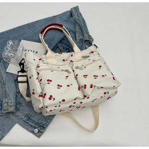 Detail of white tote bag with red cherry print, dual front zip pockets and wide strap