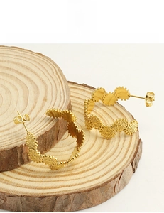 Macro de boucles d'oreilles fleur en acier plaqué or 18k sur un support en bois