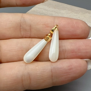 Colgantes de concha blanca en forma de gota con aros dorados mostrados sobre la mano