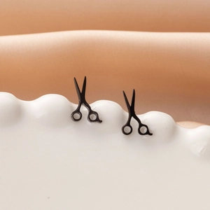 Detail view of matte black scissor stud earrings on white ceramic tray over silk