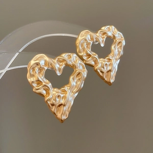 Macro shot of irregular lava texture gold heart hoop earrings with hollow design