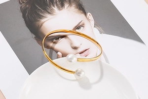 Close-up of a minimalist gold open bangle with two white pearls on a white ceramic plate