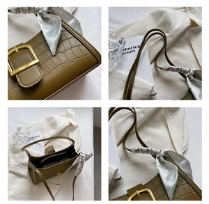Detail of green crocodile embossed handbag featuring a silk scarf and metallic buckle
