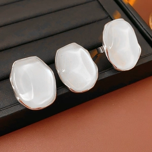Detailed view of three adjustable silver rings with oval white resin stones on black leather