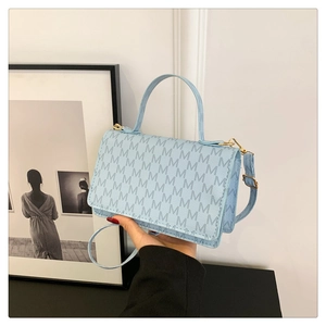 Detail view of light blue crossbody bag with repeating letter pattern and gold hardware
