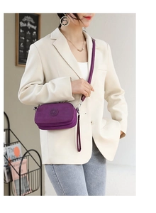 Purple nylon crossbody bag worn by a model in a minimalist home setting