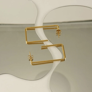 Detailed view of golden rectangular earrings on a reflective surface with a wave texture