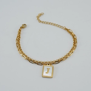 Detalle de pulsera dorada con eslabones de clip y colgante cuadrado de nácar con la letra J