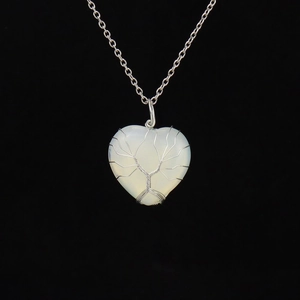 Macro detail of a silver wire-wrapped Tree of Life on a white heart stone pendant
