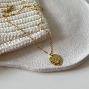 Detailed view of a gold heart pendant necklace with a small sparkling rhinestone on a white tray