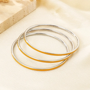 Detail of three stackable silver bangles with yellow enamel inlay on white fabric