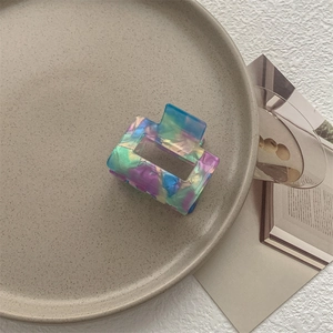 Dettaglio di pinza per capelli quadrata con texture marmorea colorata su piatto beige