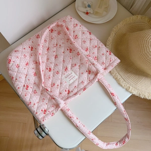 Detail of pink floral quilted tote bag with intricate stitching and brand woven label