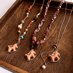 Detailed view of hand-woven rocking horse necklaces with mixed beads on dark wood tray