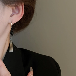Detail view of long geometric drop earrings with black beads and silver metal on model