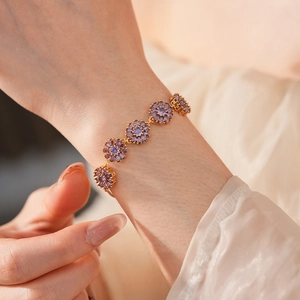 Close-up of a gold-plated bracelet featuring purple zircon flower charms on a model's wrist
