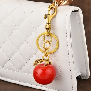 Red apple keychain charm with golden leaves on white quilted bag accessory