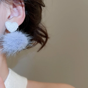 Primo piano di orecchino a cuore con pompon in ecopelliccia indossato da una modella