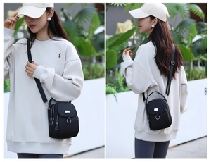 Detailed close-up of three zippered compartments and silver ring on a black nylon crossbody bag