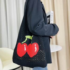 Detail of black knit tote bag with red cherry pattern shown on shoulder for capacity