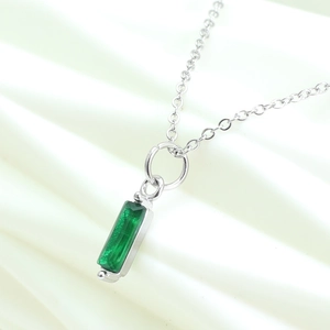 Macro shot of a silver necklace with a rectangular emerald green zircon pendant on white fabric
