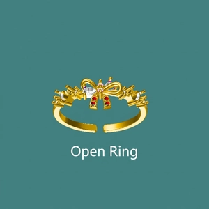 Golden open bow ring with red and clear zircon stones on a teal background