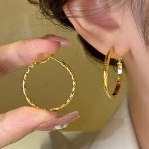 Détail de grandes créoles géométriques dorées avec finition de texture martelée