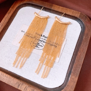 Detail of elegant gold tassel earrings with multi-layer bead chains in a wooden tray